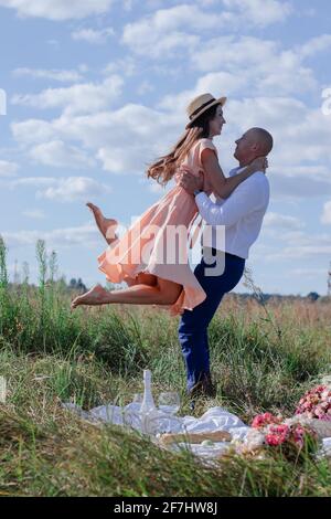 happy couple dancing in the field. brunette in cream dress and bald man in white shirt and blue pants. husband and wife on a romantic date. love story Stock Photo