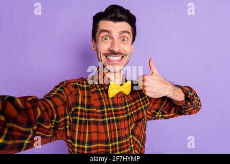 Photo of impressed funny young guy wear plaid shirt showing thumb up recording video isolated violet color background Stock Photo