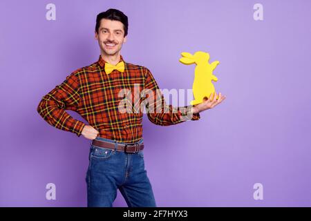 Photo of funny sweet young man dressed checkered shirt holding yellow easter bunny isolated purple color background Stock Photo