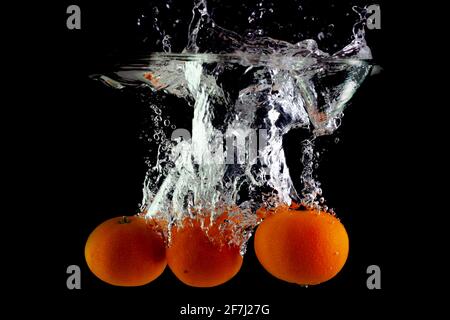three juicy tangerines in water on a black background Stock Photo