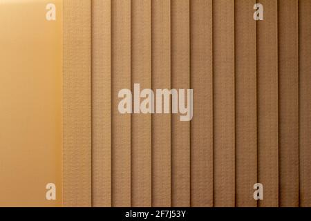 Full frame abstract art design background of vertical window blinds along a textured wall, in a gradient shade of beige Stock Photo