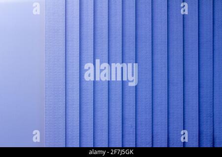 Full frame abstract art design background of vertical window blinds along a textured wall, in a gradient shade of blue Stock Photo