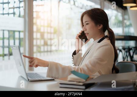 Banker telling to client regarding bank services make recommendations via cell phone while pointing at laptop. colleagues talking, working on project Stock Photo