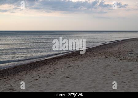 Sandy coastline covered with wavy tracks goes into perspective diagonally, azure sea with smooth surface reflecting clouds in calm weather connects wi Stock Photo