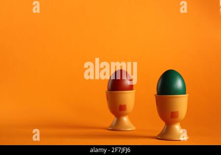 Two easter colored painted traditionally eggs into eggcups clsoe up on orange background. Stock Photo
