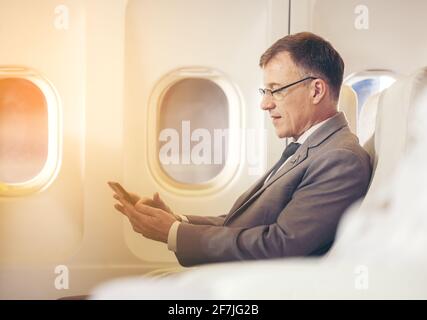 businessman with suit sitting seat via using smartphone in the airplane Stock Photo