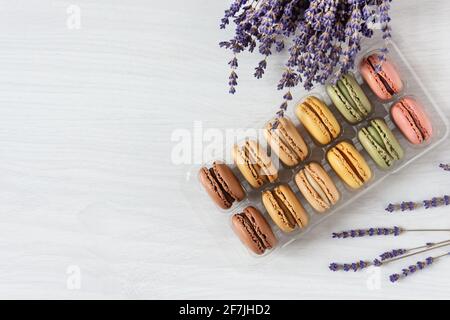 Multi colored french macaroons in a box top view on white wooden background. French meringue cookie macarons. Stock Photo