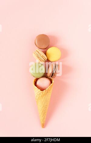 Variety of macaroons in a waffle ice cream cone on pink background top view.  Creative composition of french meringue cookie macarons. Stock Photo