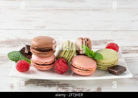 Variety of french macaroons with raspberry, blueberry, mint leaf and chocolate on a plate over wooden background. French meringue cookie macarons and Stock Photo