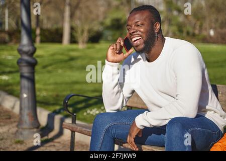 Happy black man talking on smart phone sitting in a park on a sunny day. High quality photo Stock Photo