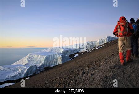 Hikers enjoying the sunrise by a glacier at Stella Point near by the summit of the UNESCO World Heritage Site of Mount Kilimanjaro in Tanzania, Africa Stock Photo