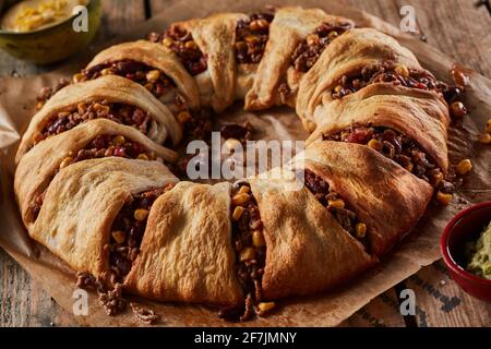 Closeup of appetizing baked Mexican dish enchilada crescent ring made with tortillas and filled with meat and corn and beans served with sauces Stock Photo