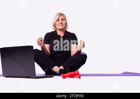Happy old middle aged senior 50s woman learning to meditate at home watching live online tv yoga class tutorial on website looking at laptop pc doing Stock Photo