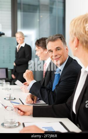 Business - presentation within a team, a female, colleague is standing on the flipchart, one man is looking into the camera Stock Photo