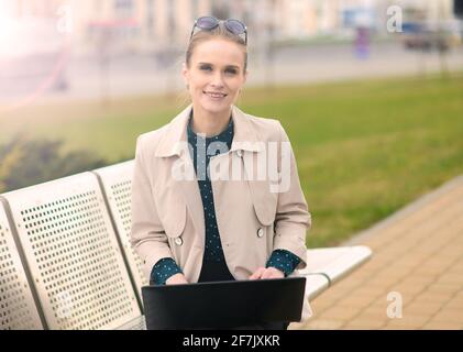 Happy beautiful businesswoman with sunglasses, phone, laptop, cup of coffee in the city street Stock Photo