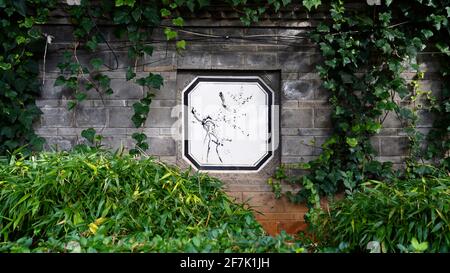 A Chinese style brick wall with painting and ivy on it, also grasses growing below. Stock Photo