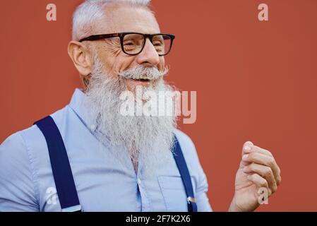 Older caucasian hipster man with prescription glasses and beard smiles happy outdoors in the city - Focus on face. Stock Photo