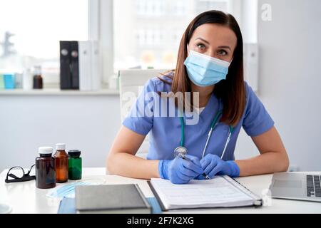 Portrait of female doctor sitting at desk in protective mask Stock Photo