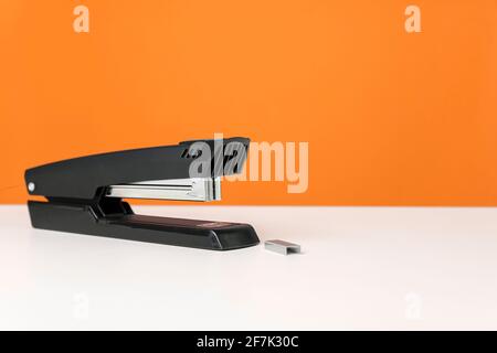 Stapler on white table against bright orange background. Minimalistic, vivid colors. Office supplies. Stock Photo