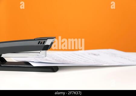 Stapler on white table against bright orange background. Minimalistic, vivid colors. Office supplies. Stock Photo