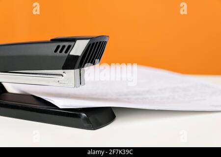Stapler on white table against bright orange background. Minimalistic, vivid colors. Office supplies. Stock Photo