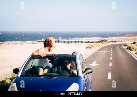 Car travel friends transportation two happy woman ejoy convertible auto together in summer trip holiday vacation - ocean and beach in background - dri Stock Photo