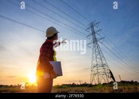 High voltage, construction electrical engineer or technician standing and watching at the worker checking location site near to High voltage tower. Stock Photo