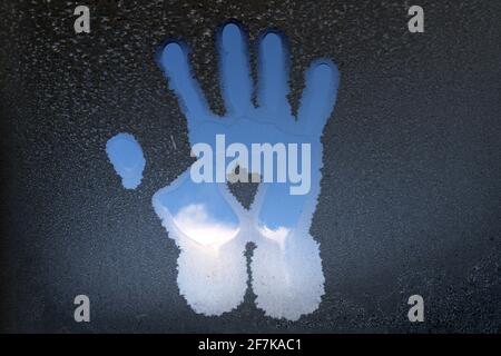 Track of the palm of hand on the glass covered with frost. The palm melted the ice on the glass. Stock Photo