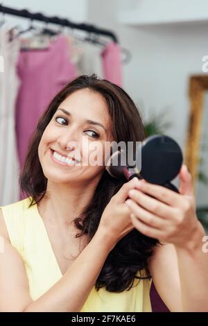 Young latin girl putting on makeup in front of the mirror applying makeup base with a brush Stock Photo