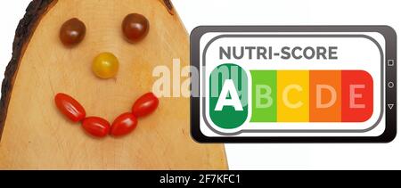 Nutri-Score logo on a mobile phone display next to a laughing face made of tomatoes on a wooden board. Nutri-Score is a nutrition labelling system for Stock Photo