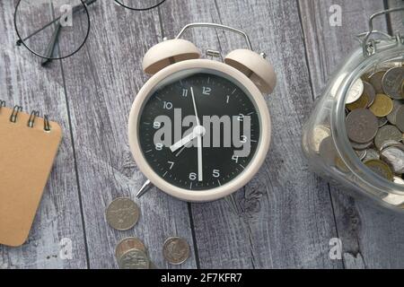old alarm clock , notepad and coins on wooden table  Stock Photo