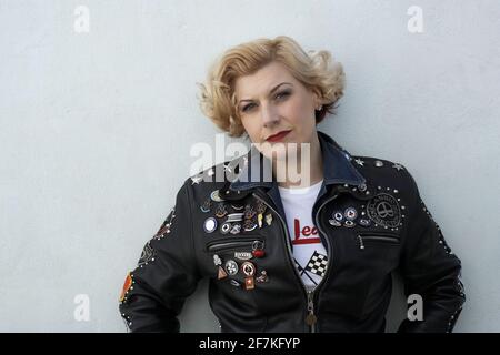 Beautiful blond female biker ,cafe racer wearing a leather jacket covered in studs, patches and badges.