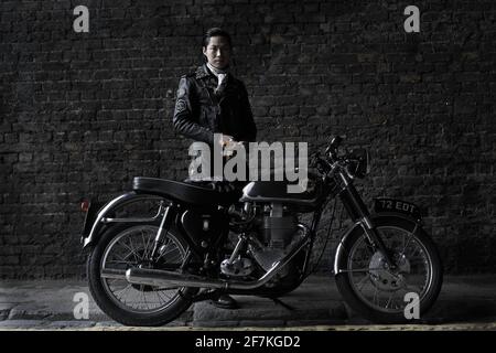 biker , cafe racer wearing black leather jacket standing behind classic british motorcycle in London , UK Stock Photo