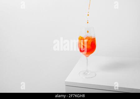 Aperol Spritz Cocktail. Pouring aperol in wine glass with ice on white background. Long fizzy drink. Minimal creative concept.