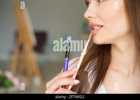 Portrait of talented young woman painting picture in art studio with inspiration. Stock Photo