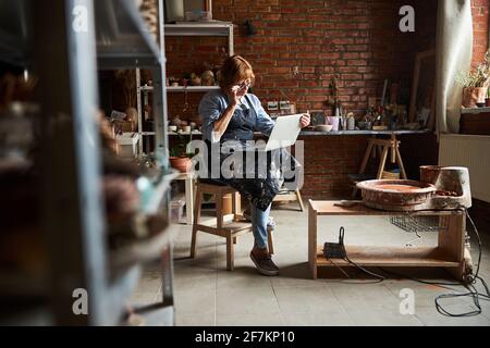 Charming senior woman using laptop in pottery workshop Stock Photo