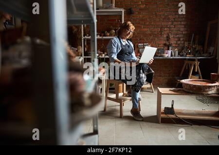 Nice elderly woman using laptop in pottery workshop Stock Photo