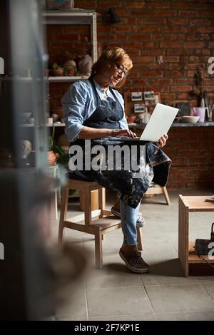 Nice senior woman using notebook in pottery workshop Stock Photo