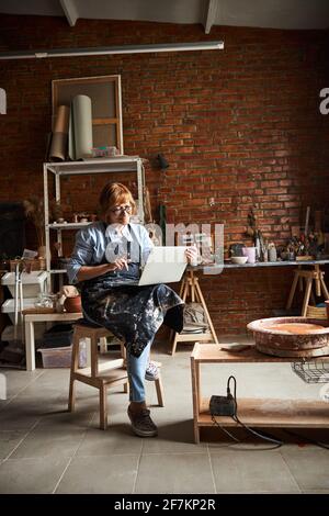 Nice female potter using notebook in pottery workshop Stock Photo