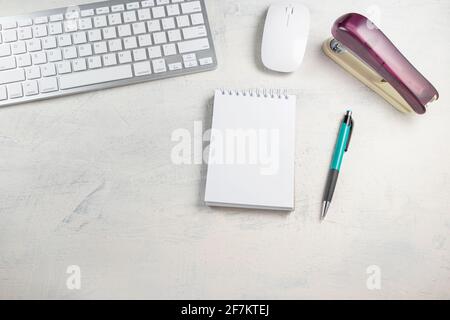 Desktop top view. Blank notepad with pen, keyboard, mouse and stapler on the desktop. Mockup Stock Photo