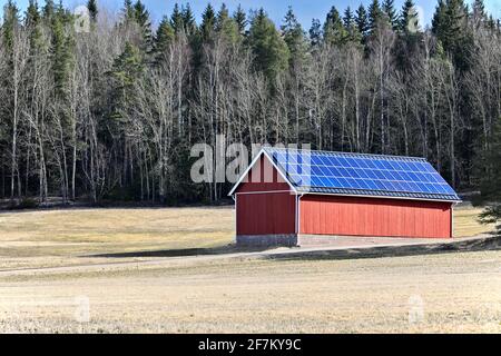 Solar panels on rooftop of a red outbuilding in rural Finland on a sunny day of spring. Stock Photo