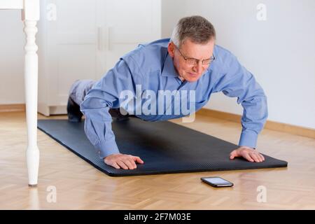 Mature businessman doing push ups at home - selective focus on the face Stock Photo