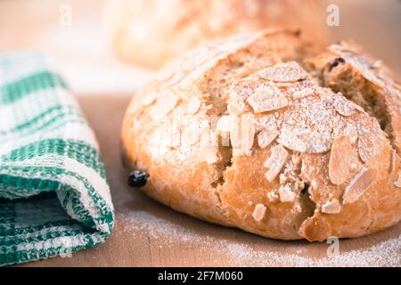 Freshly baked, homemade sweet cake with almonds and raisins on a wooden board. Easter loaf. Green cloth. Delicious snack. Stock Photo