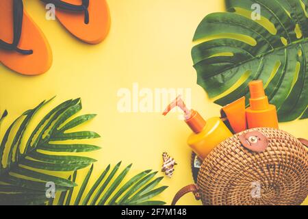Sunscreen bottles arranged in straw bag on a bright yellow background with palm leaves, top view Stock Photo
