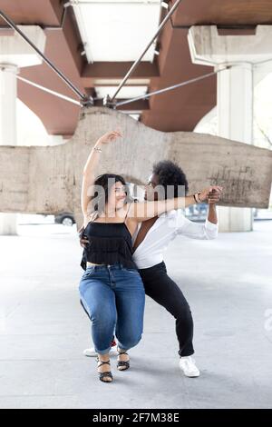 Young multiracial couple dancing together passionately on a downtown street. Space for text. Stock Photo