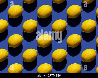 Rhythmic pattern of lemons on a blue background. Hard shadows. Stock Photo
