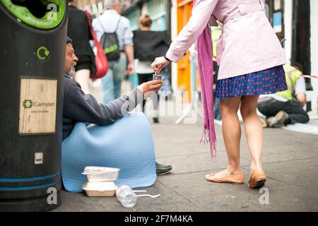 Young woman handing spare change to jobless elderly man begging on high street. Simple acts of kindness. Camden High St, London, UK. Aug 2015 Stock Photo