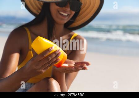 Smiling mixed race woman on beach holiday using sunscreen cream Stock Photo