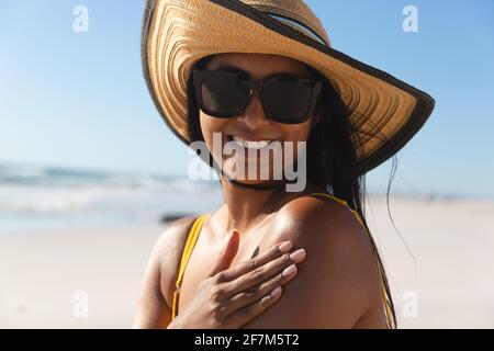 Smiling mixed race woman on beach holiday using sunscreen cream Stock Photo