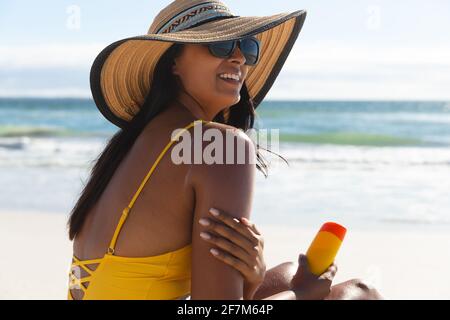 Smiling mixed race woman on beach holiday using sunscreen cream Stock Photo